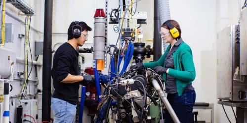 Photo of Carrie Hall and student working on an engine in the lab